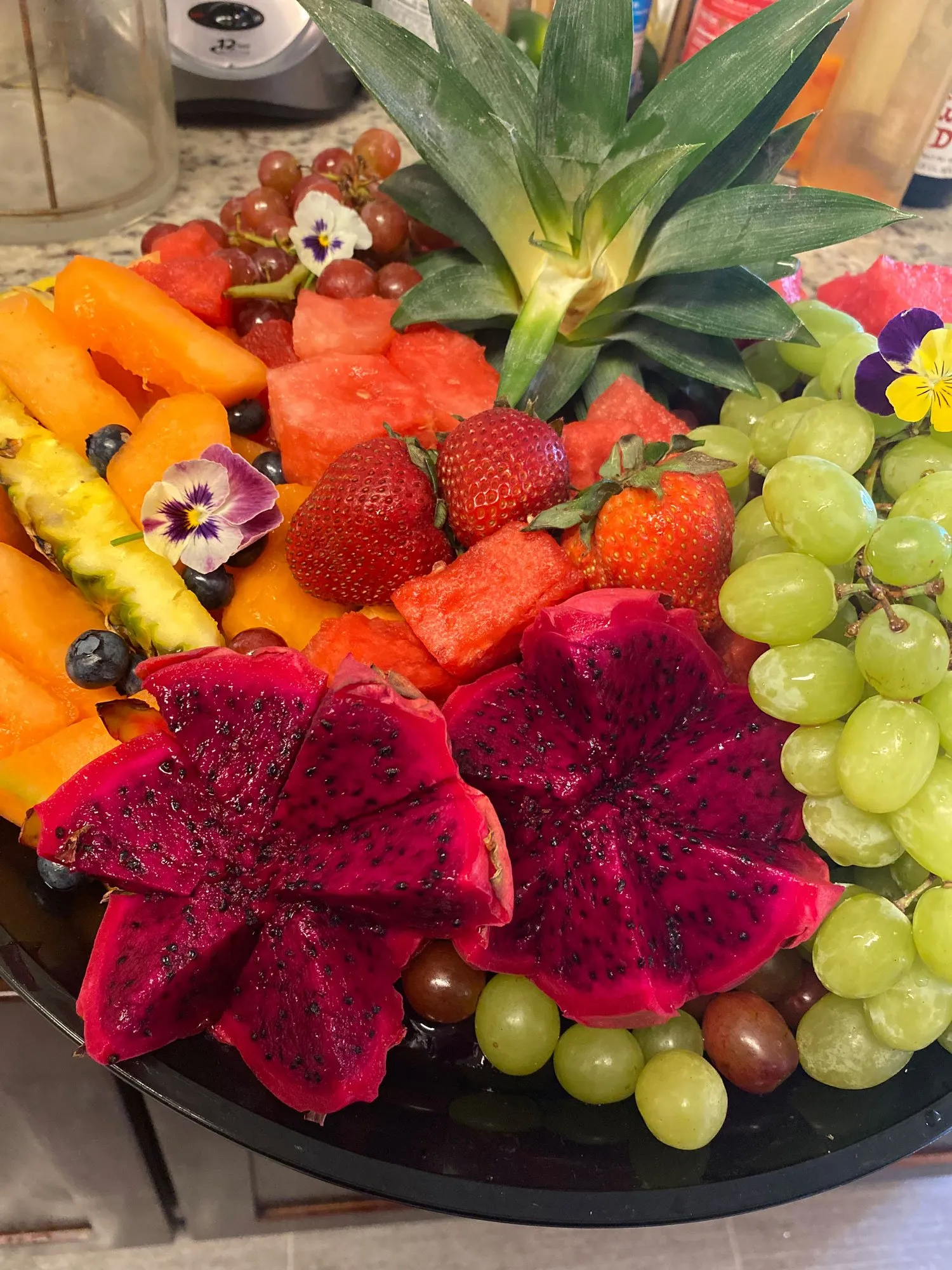 Fruit platter of dragon fruit, strawberries, watermelon, cantaloupe and green grapes around a pineapple crown